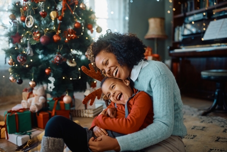 A mother hugging her young child in a decorated living room with a Christmas tree, capturing a joyful holiday moment while discussing holiday custody schedules.